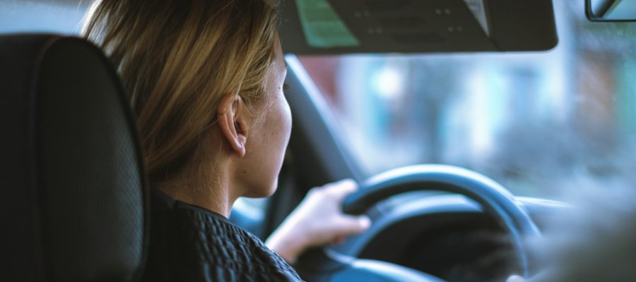 Young woman with blonde hair driving a car, both hands on the steering wheel, focused on the road ahead